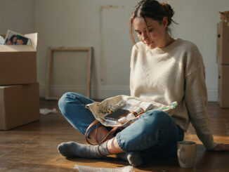Déménagement : image ou photo d'une personne assise au milieu de cartons de déménagement, tenant un petit sac ouvert avec des objets essentiels visibles : clés, téléphone, chargeur, documents, médicaments et brosse à dents.