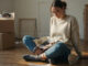 Déménagement : image ou photo d'une personne assise au milieu de cartons de déménagement, tenant un petit sac ouvert avec des objets essentiels visibles : clés, téléphone, chargeur, documents, médicaments et brosse à dents.