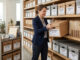 Transfert des archives : image ou photo d'une personne dans un bureau moderne, en train de déplacer des boîtes d’archives bien étiquetées, avec des dossiers rangés proprement sur une étagère. L’ambiance doit être claire, professionnelle et rassurante. On peut voir un chariot avec des cartons, quelques classeurs, et une lumière douce pour donner une impression d’organisation et de sérénité.