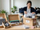 Matériel informatique : image ou photo d'un bureau en cours de déménagement avec un ordinateur portable, un écran, un clavier et des câbles bien rangés dans des cartons ouverts. On voit aussi du papier bulle, des étiquettes “fragile” et une personne qui emballe soigneusement un écran.